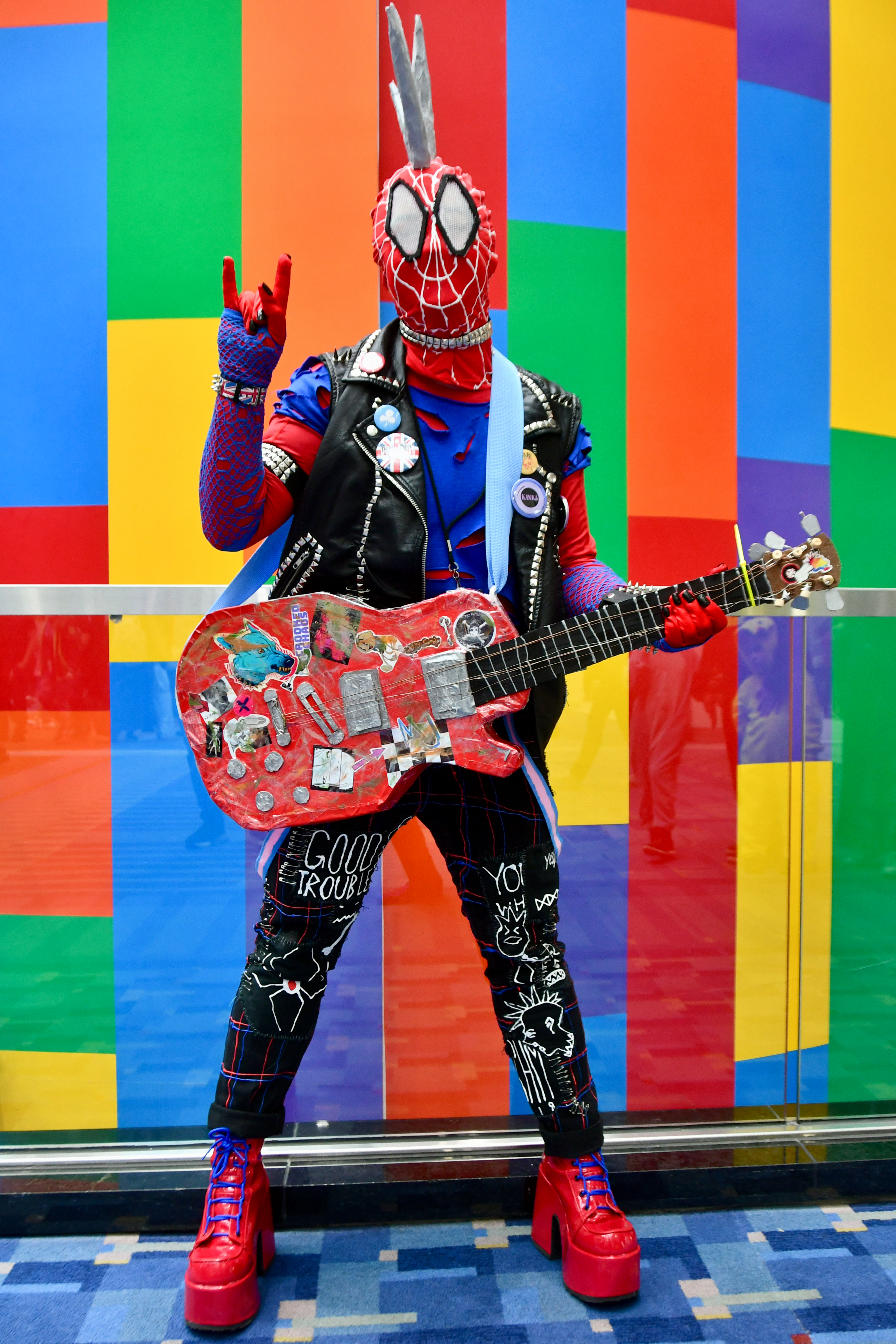 Spider-Punk cosplayer standing in front of a colorful wall, holding a prop guitar