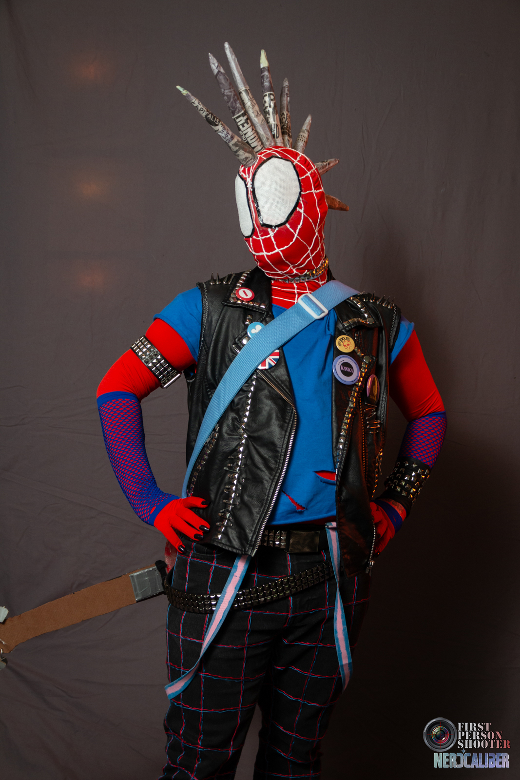 Spider-Punk cosplayer poses with their hands on their hips and guitar slung across their back