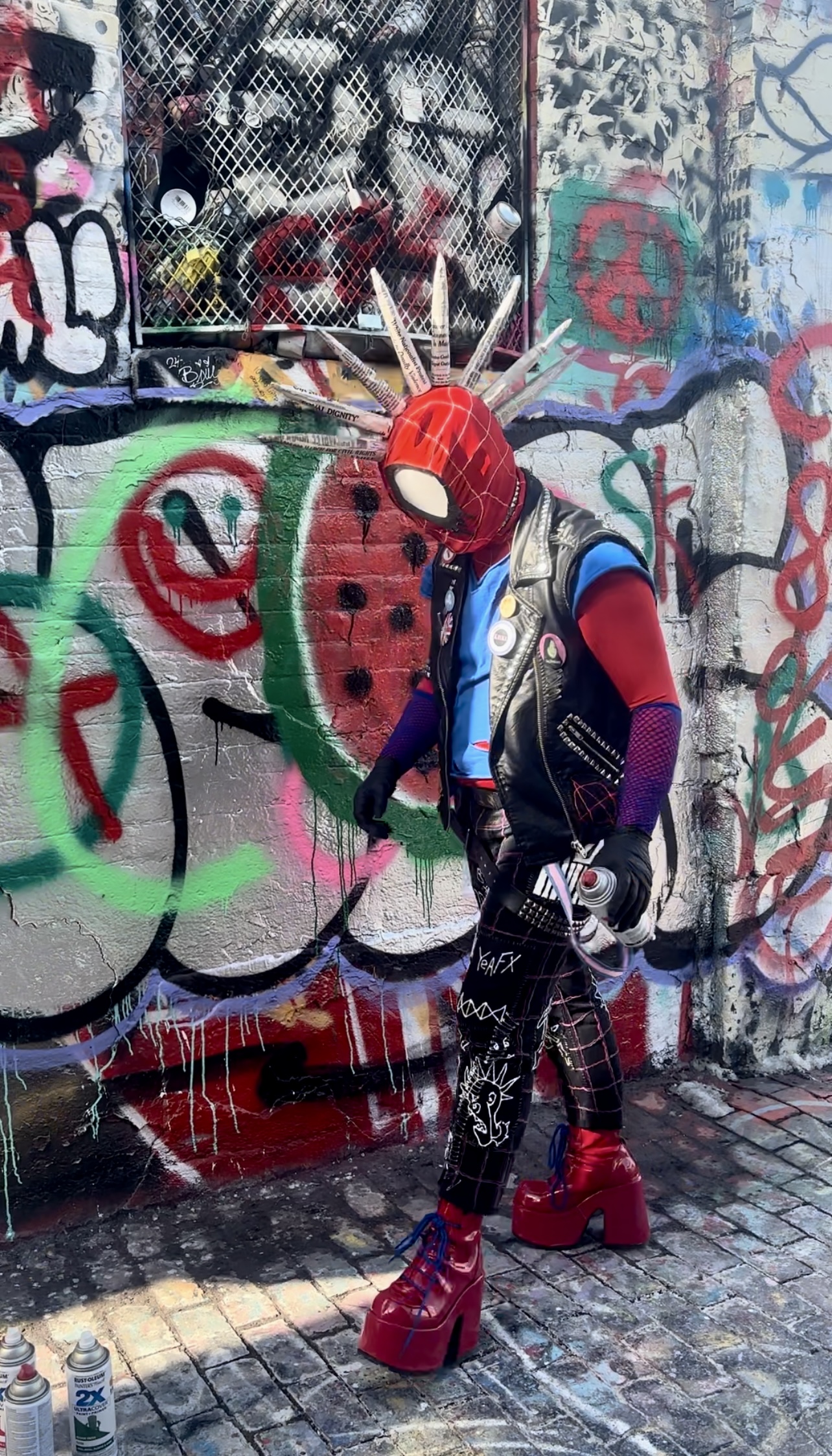 Spider-Punk cosplayer walking by a graffiti wall, in front of a spray-painted watermelon design