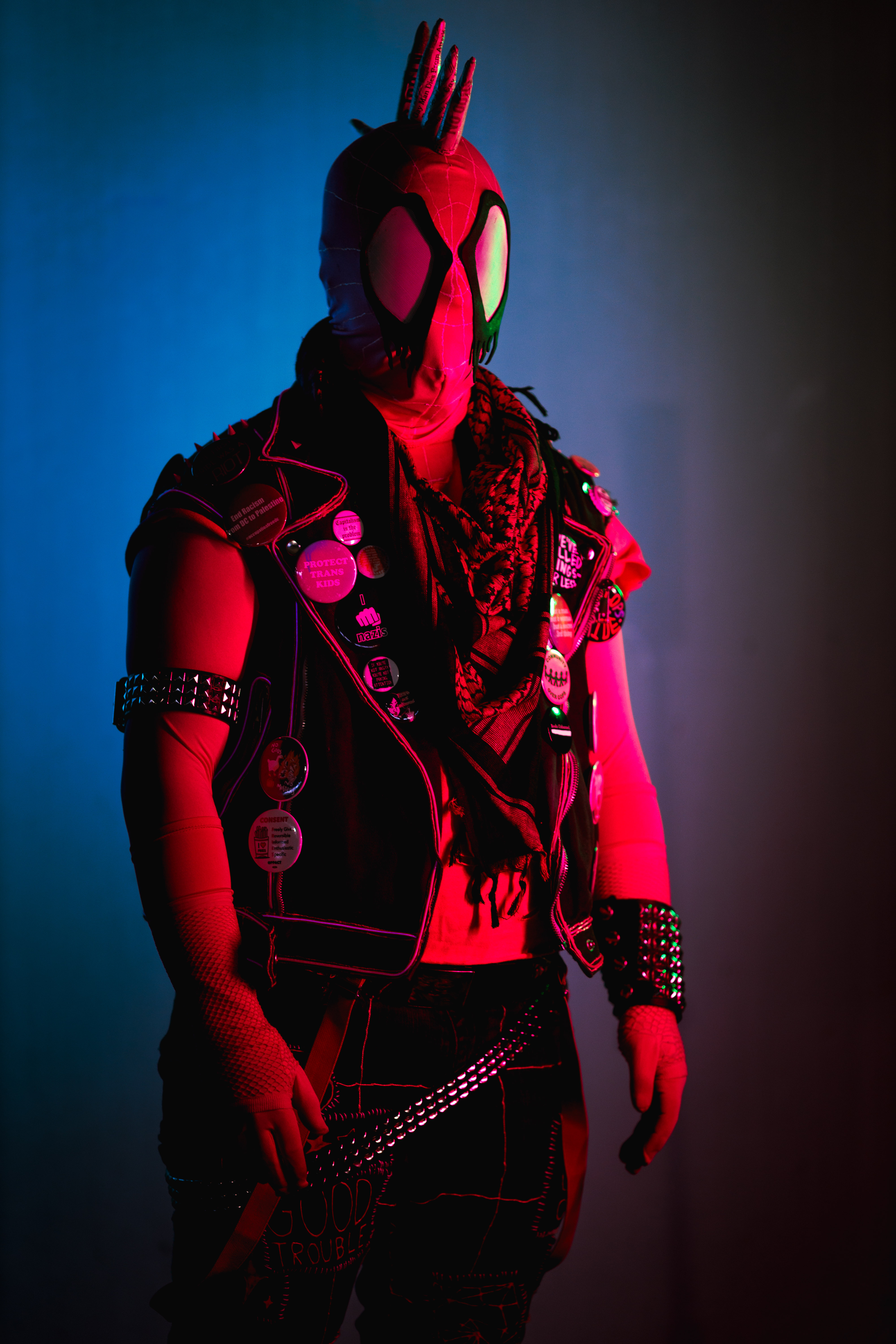 Spider-punk (pink palette) cosplayer wearing a pink keffiyeh, illuminated by colorful light