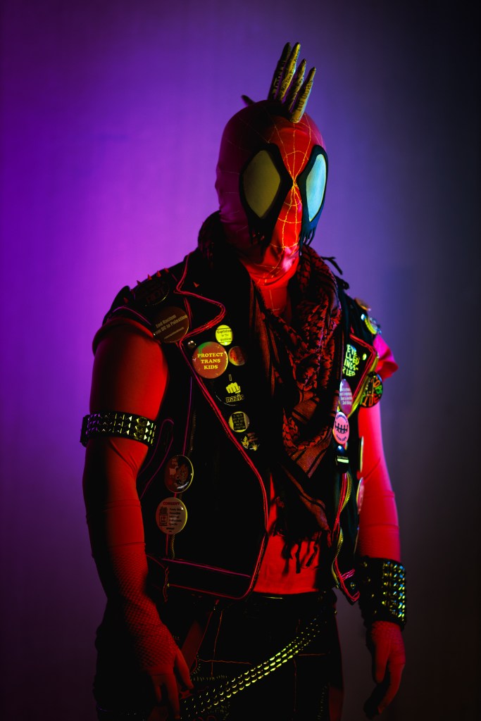 Spider-punk (pink palette) cosplayer wearing a pink keffiyeh, illuminated by colorful light