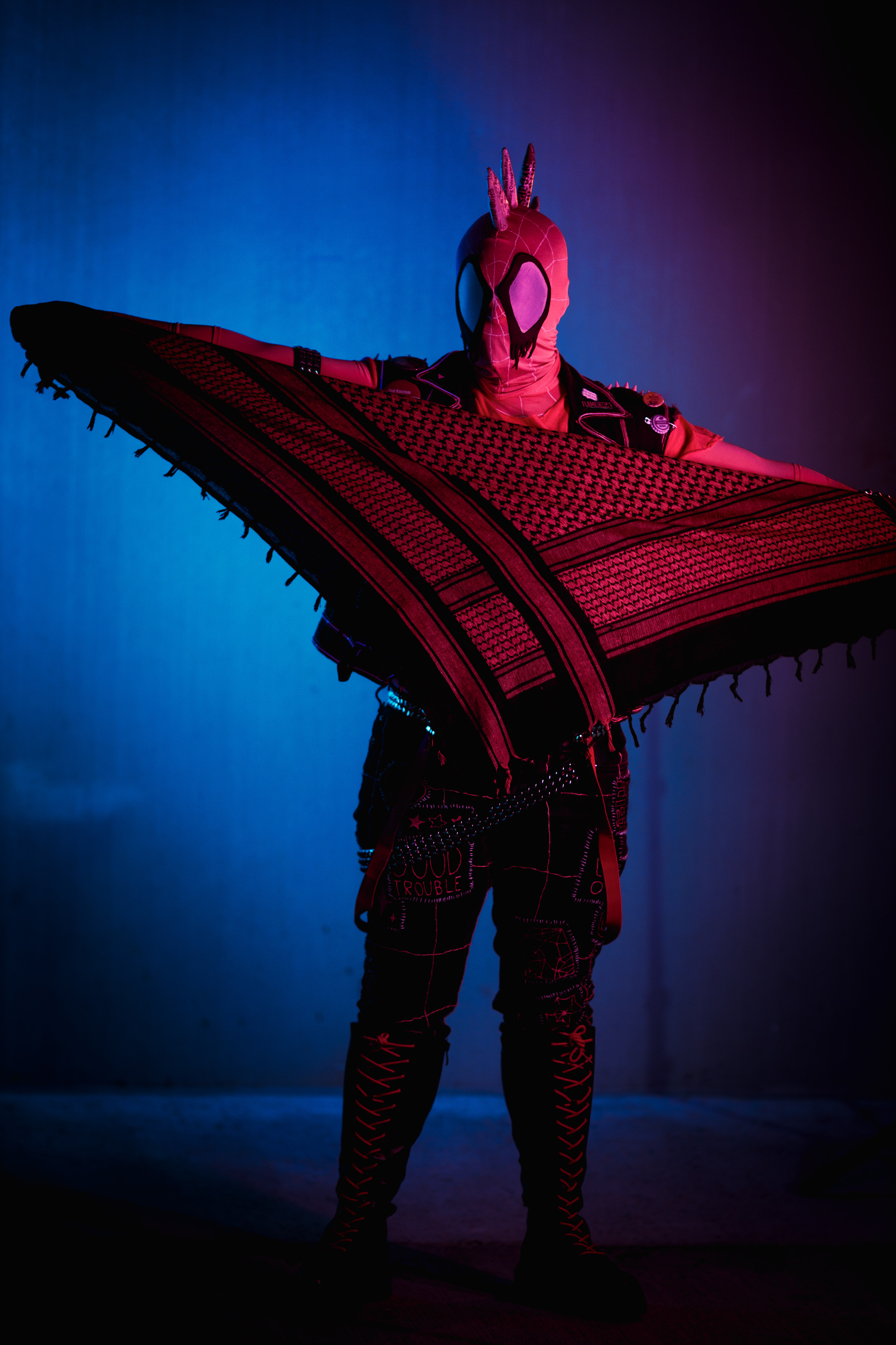 Spider-punk (pink palette) cosplayer holding a pink keffiyeh, illuminated by colorful light
