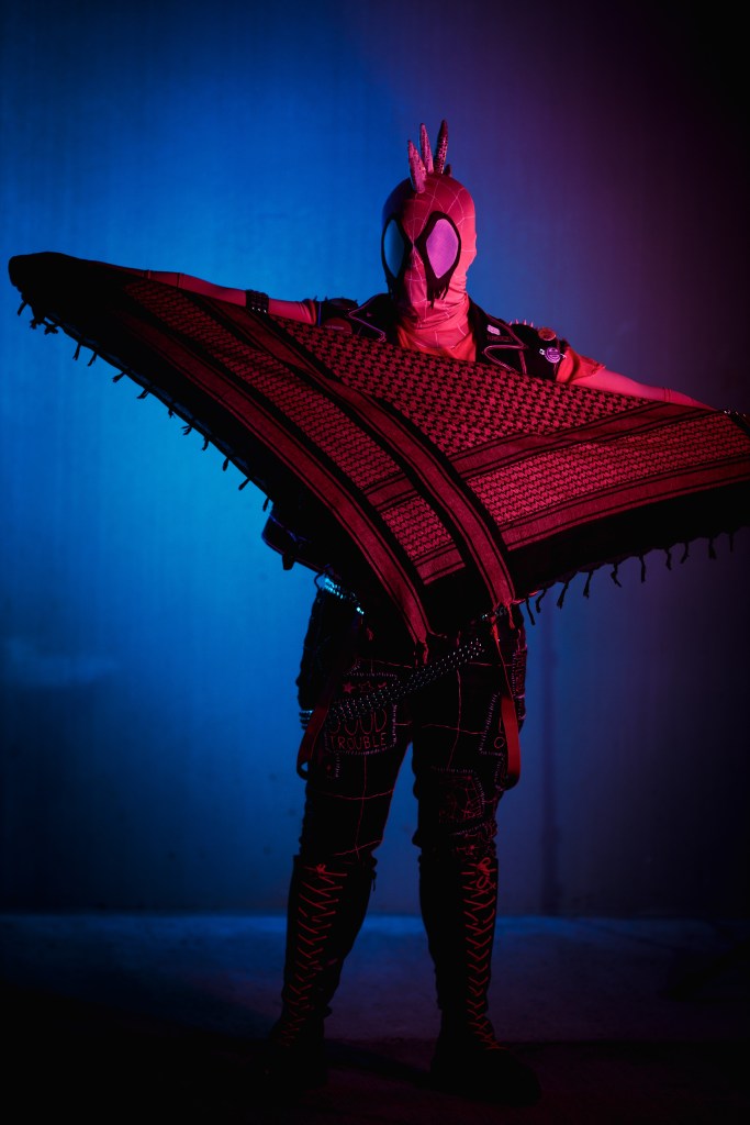 Spider-punk (pink palette) cosplayer holding a pink keffiyeh, illuminated by colorful light