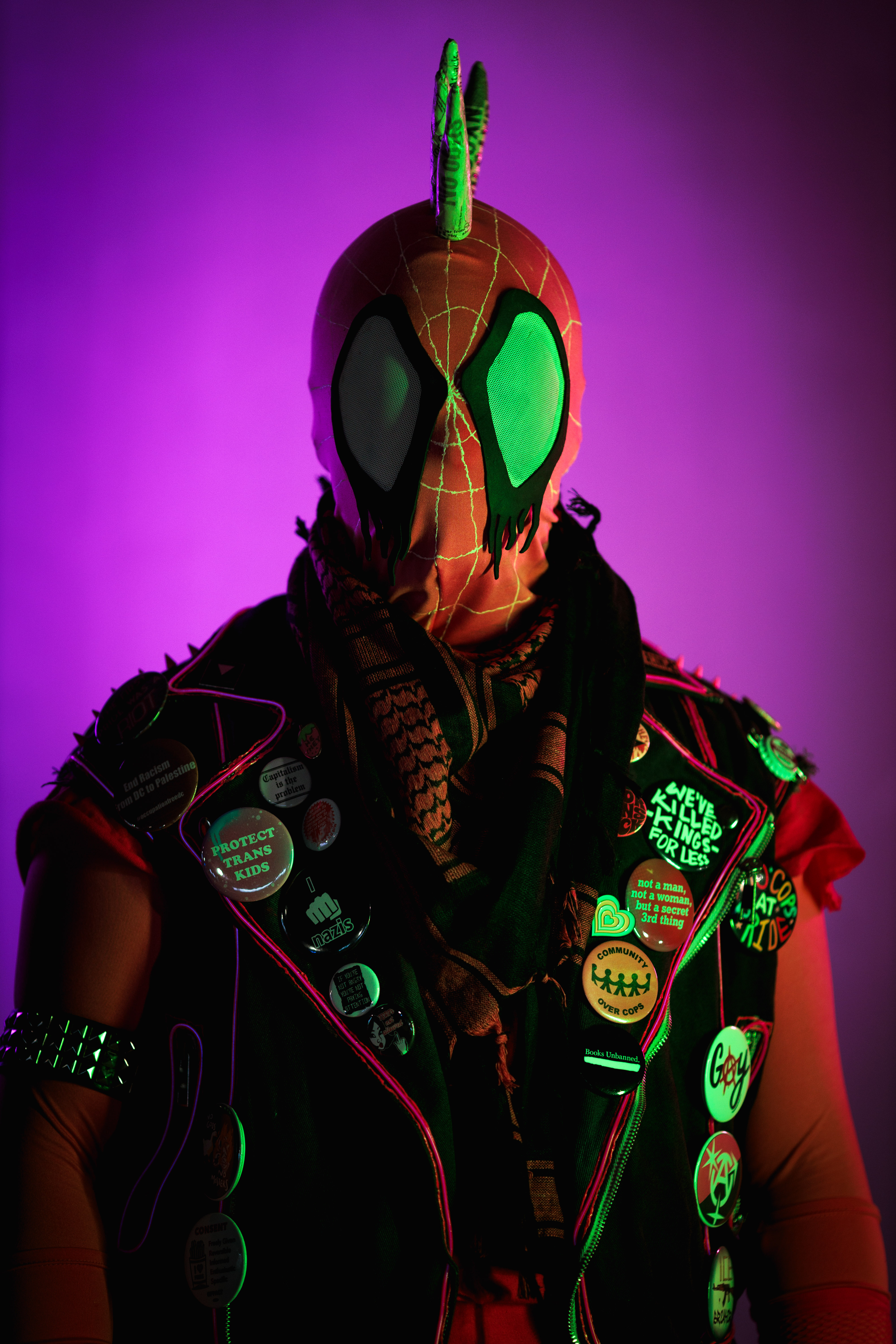 Spider-punk (pink palette) cosplayer wearing a pink keffiyeh illuminated by purple-pink light