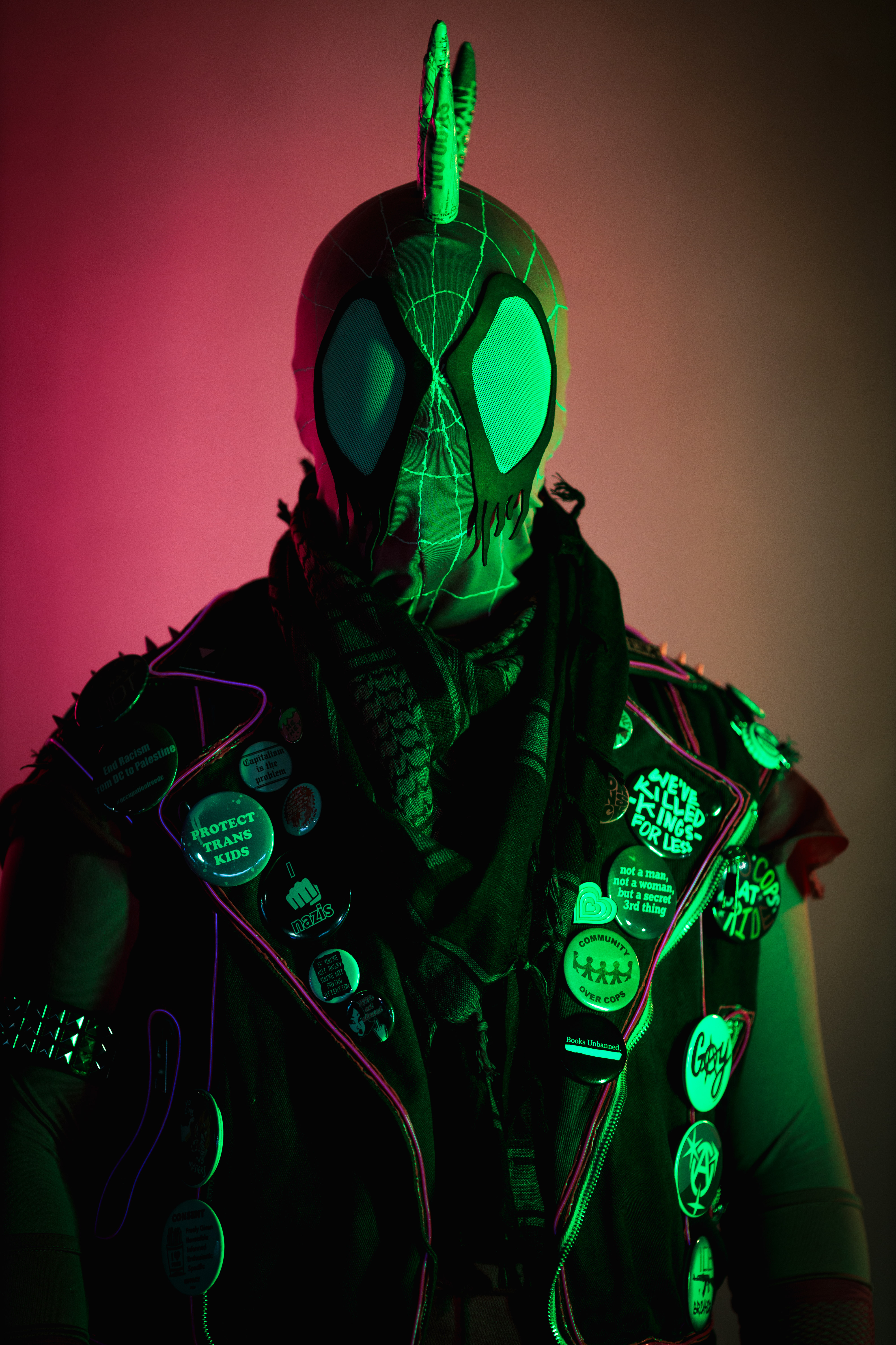 Spider-punk (pink palette) cosplayer wearing a pink keffiyeh illuminated by pink light on the left and warm light on the right